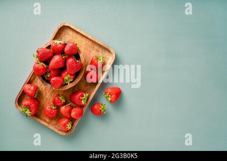 Fraise fraîche sur fond bleu. Fraises avec feuilles sur assiette en bois. Banque D'Images