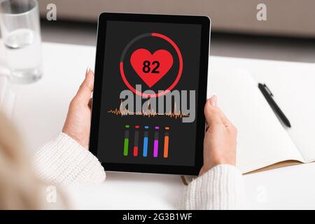 Femme méconnaissable qui fait une pause au travail à la maison, qui utilise la toute dernière application de santé sur une tablette numérique, qui vérifie la fréquence cardiaque et les gros plan. Technologies modernes Banque D'Images