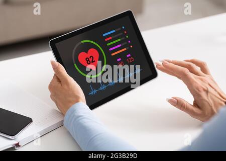 Mains de femme tenant un bloc noir avec application de santé à l'écran, femme méconnaissable vérifiant son rythme cardiaque tout en passant du temps à la maison, en utilisant HEAL Banque D'Images