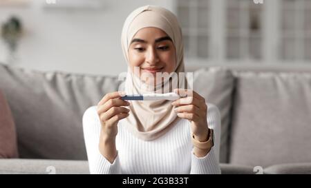 La santé féminine, l'ovulation, l'attente de bébé et de bonnes nouvelles. Portrait en gros plan de heureuse heureuse jolie femme arabe millénaire dans hijab regardant le preg positif Banque D'Images