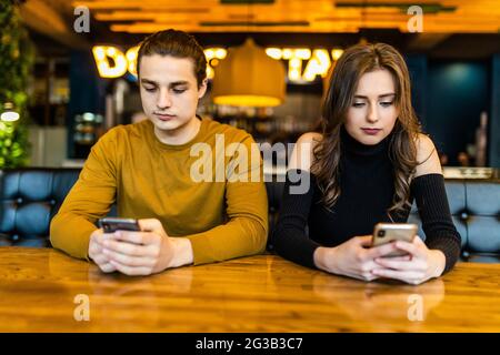 Phubbing, toujours connecté, la dépendance à internet, young couple in cafe à à leurs smartphones, social network concept Banque D'Images