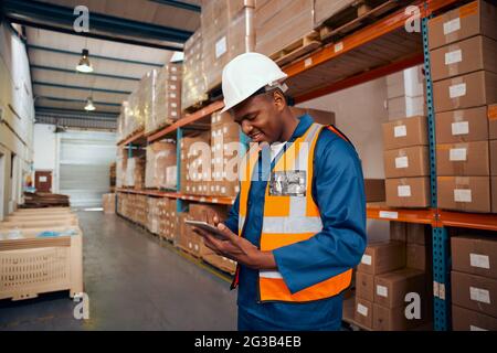 Un superviseur souriant qui vérifie les enregistrements de stock sur une tablette numérique à proximité de la pile de boîtes Banque D'Images