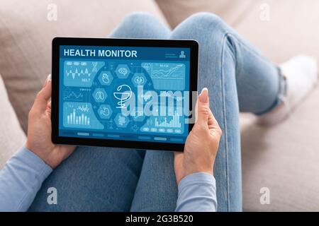 Une femme méconnaissable utilise une application mobile de surveillance de santé sur une tablette numérique tout en se reposant sur un canapé à la maison, en vérifiant son état de santé pendant son séjour Banque D'Images