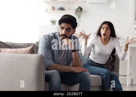 Querelle, scandale à la maison, conflit, problèmes de relations, divorce. Une jeune femme arabe agitée en colère hurle et fait des gestes contre un mari offensé, ignorant Banque D'Images