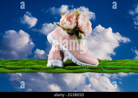 Chaussures roses pour femmes en tissu doux et léger. Les chaussures reposent sur l'herbe verte avec un bouquet de fleurs à l'intérieur contre le ciel bleu. Banque D'Images