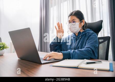 Une jeune fille asiatique porte un geste de masque de salutation étudiant apprenant en ligne avec un casque et un ordinateur portable à la maison Banque D'Images