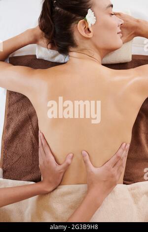 Vue en grand angle de la jeune femme qui s'est allongée sur une table de massage et qui se fait masser Banque D'Images