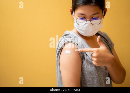 Gros plan des jeunes filles heureux et porter un masque dans l'épaule avec du plâtre sur le bras après la vaccination sur fond jaune studio, fille thaïlandaise, vaccinée Banque D'Images