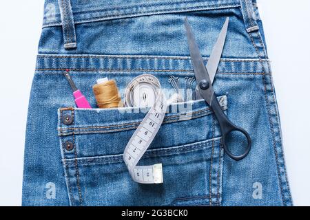 Gros plan de la défonceuse de couture, filetage, ruban centimètre, jeu, goupilles, Ciseaux dans la poche de Blue Jeans sur fond blanc vue de dessus. Banque D'Images