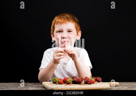 un garçon aux cheveux rouges mangeant des fraises Banque D'Images