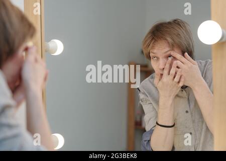 Jeune homme mettant la lentille de contact devant le miroir en studio Banque D'Images