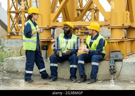 Groupe de constructeurs parlant tout en déjeunant sur le chantier de construction Banque D'Images