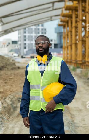 Jeune homme africain constructeur en uniforme debout sur le chantier de construction Banque D'Images
