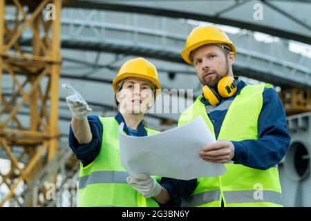 Deux constructeurs confiants avec un plan de discussion sur le chantier de construction Banque D'Images