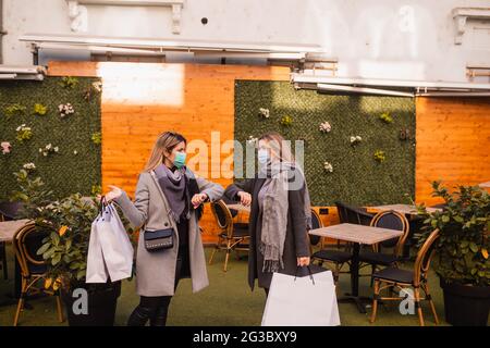 Deux belles jeunes femmes blondes avec des masques médicaux se saluent les unes les autres avec leurs coudes dans la ville.Shopping pendant le coronavirus COVID-19 Banque D'Images