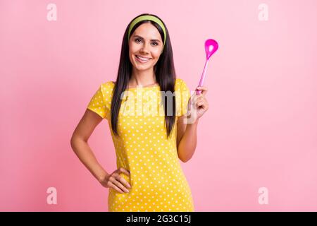 Photo de la jeune femme au foyer positive tenir cuillère main taille beau sourire isolé sur fond rose pastel Banque D'Images