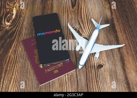 Smartphone avec logo de l'application Momondo avec jouet avion et passeport rouge sur fond de bois. Demande de voyage, planification des vacances Banque D'Images