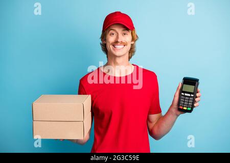 Portrait de livreur positif tenir deux boîtes pos terminal porter chapeau isolé sur fond bleu Banque D'Images