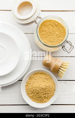 Concept de lavage de la vaisselle avec de la moutarde en poudre. Plaques blanches propres avec bol et bol de poudre de moutarde jaune et brosse à vaisselle en bois et classe Banque D'Images