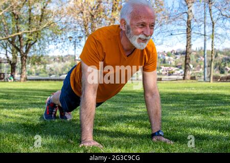 Portrait d'un homme âgé qui fait de l'exercice, qui fait des exercices dans le parc. Un homme âgé en bonne forme avec des bras forts. Banque D'Images