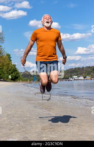 Homme âgé actif, sautant la corde, s'exerçant sur la plage au bord de la rivière. Banque D'Images