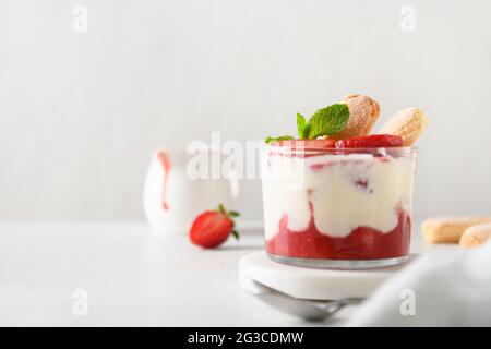 Dessert estival en pots en verre avec biscuits savoyardi, mascarpone et fraises à la crème fouettée. Gros plan. Tiramisu italien avec somme Banque D'Images