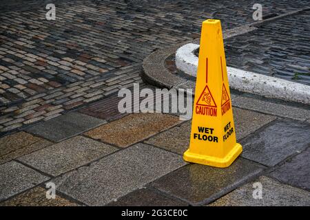 Cône jaune avec signe de surface glissante avec précaution, sur les carreaux de pierre humides Banque D'Images