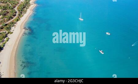 Haute vue aérienne des bateaux de loisirs à l'ancre et d'un hors-bord qui se déplace vers la rive en face d'une plage de sable tropical parsemée de rochers Banque D'Images