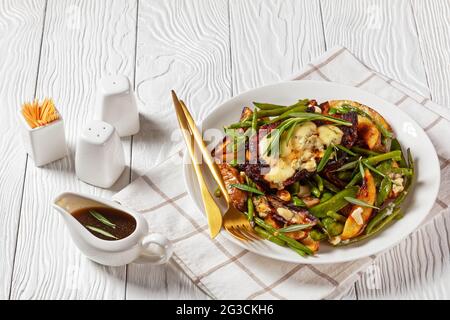 steak de porc recouvert de fromage bleu fondu sur une bande de pois mange-tout rôtis, de quartiers de pommes de terre, de haricots verts et d'ail avec sauce trempée dans un boa sauce Banque D'Images