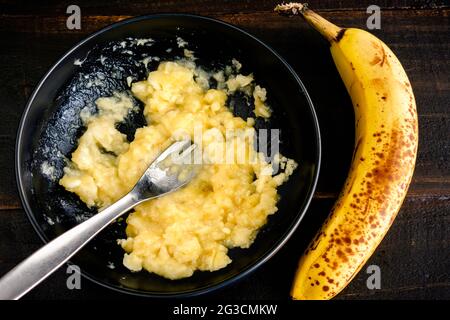 Écrasant une banane mûre avec une fourchette : un bol de banane écrasée avec une banane entière à côté Banque D'Images