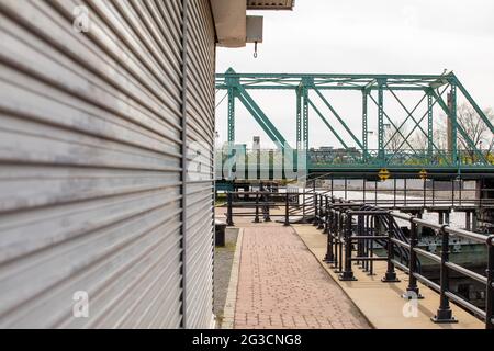 vue sur le côté d'un mur en métal sur une jetée piétonne à côté d'un canal avec un pont suspendu en métal vert au loin, par une journée nuageux Banque D'Images