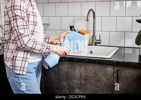 Femme de ménage nettoyant la table de cuisine et l'évier avec un chiffon bleu clair, femme méconnaissable dans une tenue décontractée ménage seul à la maison, vue latérale, court Banque D'Images