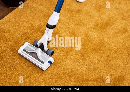 Personne méconnaissable utilisant un aspirateur à la maison, en gros plan. Nettoyage à la maison avec un aspirateur, application sur un tapis jaune Banque D'Images