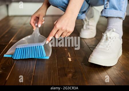 Mains de femmes balayant la poussière avec une brosse et une pelle, tenant le balai et le plancher de balayage, recueillant la poussière dans la pelle. Nettoyage des ordures.concept d'entretien ménager Banque D'Images