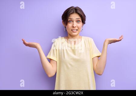 Jeune femme aux mains ouvertes demandant pardon, isolée sur fond violet. Oups. Belle dame ignorant l'expression a dit mauvaise chose regarder la caméra Banque D'Images