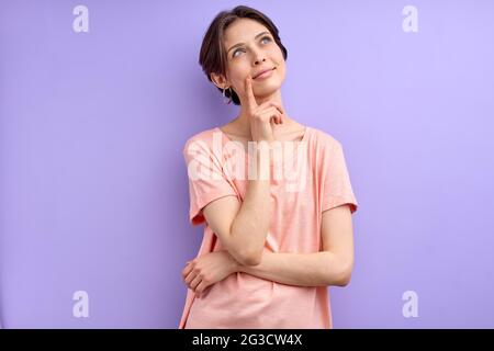 Jeune femme pensant à quelque chose, venez avec une idée, petite dame à cheveux dans l'habillement décontracté dans la contemplation, tenant le doigt sur le menton Banque D'Images