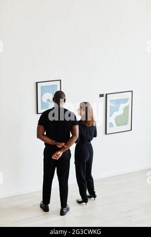 Vue minimale en grand angle sur un couple élégant qui regarde des peintures dans une galerie d'art moderne, un espace de copie Banque D'Images