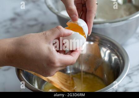 La main d'une femme fendre un œuf sur un bol en métal rond à la lumière naturelle Banque D'Images