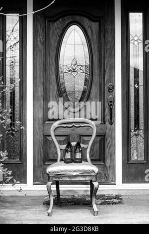 Photo verticale en niveaux de gris de chaussures sur une ancienne chaise, devant une porte Banque D'Images