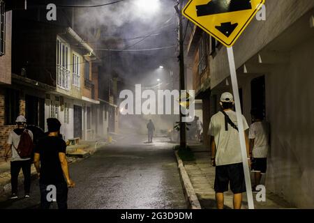 Demonstratoros jette des rochers et démystifier comme un nuage de gaz lacrymogène remplit une rue pendant que les manifestants et la police anti-émeute de Colombie (ESMAD) clash pendant la nuit du 14 juin 2021, à Yumbo - Cali, Valle del Cauca - Colombie alors que les manifestations anti-gouvernementales dévoilent dans leur 7ème semaine contre le gouvernement du président Ivan Duque, les troubles et la violence qui avaient causé au moins 70 morts. Banque D'Images