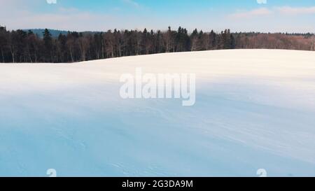 Paysage enneigé et bâclé pendant la saison hivernale. Bosquet d'arbres en arrière-plan. Journée ensoleillée et lumineuse avec la lumière du soleil sur la terre enneigée. Ciel bleu pittoresque en arrière-plan. Photo de haute qualité. Banque D'Images