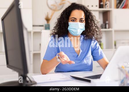 Jeune femme médecin attentif dans un masque de protection travaillant à un ordinateur portable au bureau Banque D'Images