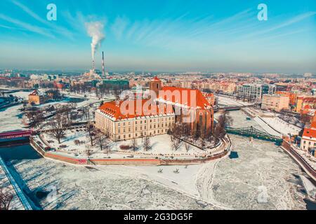 Wroclaw, Pologne 02.15.2021 - Paysage industriel enneigé avec bâtiments historiques. Cheminées de la centrale thermique en arrière-plan. Fumée polluant le ciel bleu clair. Banque D'Images