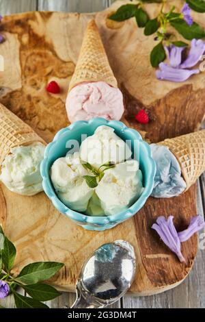 Glace à la vanille, aux myrtilles et aux framboises en cornets de gaufres et glace en tasse sur panneau de bois avec baies et fleurs Banque D'Images