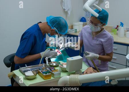 Un dentiste cambodgien et une assistante dentaire féminine, tous deux portant un masque facial et un écran de protection, travaillent sur un patient dans une clinique dentaire pendant la pandémie du coronavirus. Phnom Penh, Cambodge. 12 mai 2020. © Kraig Lieb Banque D'Images