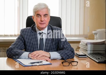 Un homme aux cheveux gris et aux cheveux gris, âgé et confiant, en costume écossais, est assis à son bureau Banque D'Images