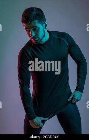 Guy en noir sportswear posant en studio sur fond gris Banque D'Images
