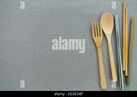 Ustensiles réutilisables et écologiques, cuillère en bambou, fourchette, baguettes, petite et grande paille en acier inoxydable sur fond beige. Banque D'Images