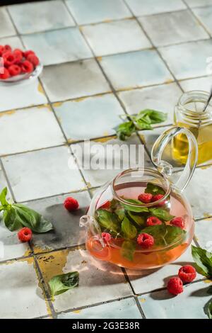 Thé chaud à la framboise dans une théière transparente sur une table en pierre. Baies fraîches, menthe, verre Banque D'Images