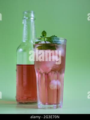 Limonade rose ou cocktail en verre et bouteille, fond vert pastel. Mise au point sélective. Banque D'Images